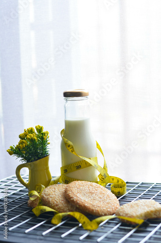A bottle of milk and low calories sesame biscuits with measuring tape: healthy lifestyle concept (selective focus image)