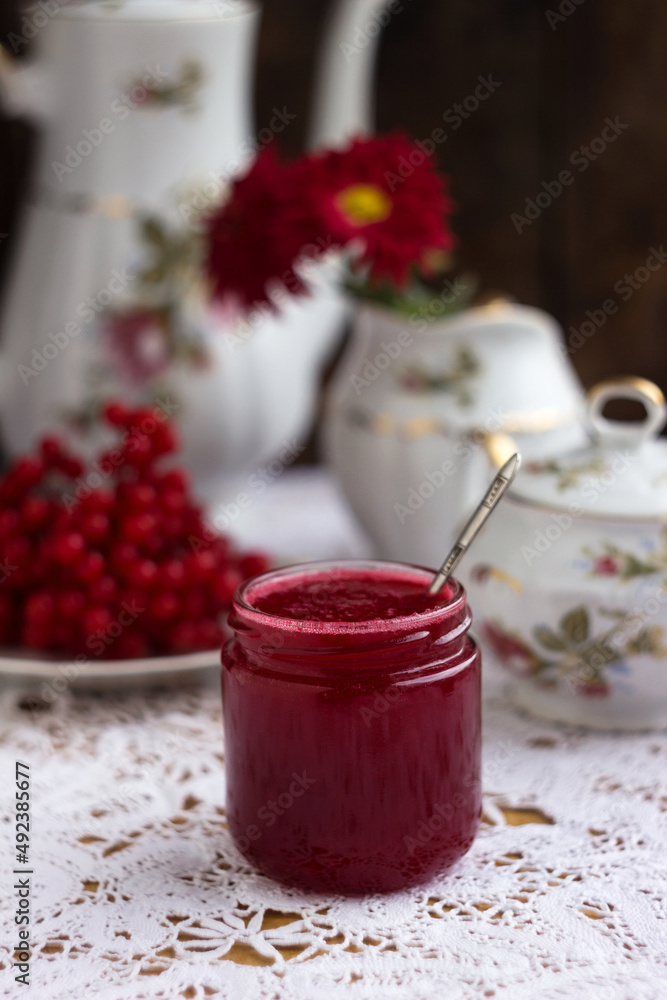 Healthy jam from viburnum berries (Viburnum opulus) in a glass jar, a bunch of viburnum, antique dishes and chrysanthemums in a vase. Preparations for the winter from colds