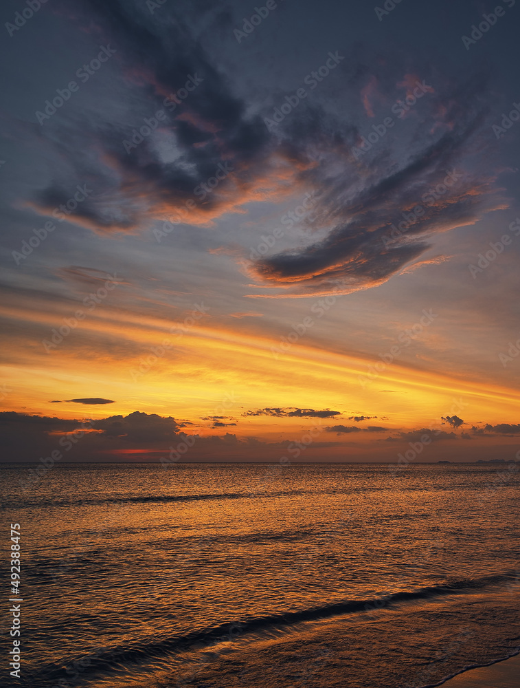 Fototapeta premium Beautiful sand beach, angel wings shape clouds in the sky during a dramatic sunset and a yacht on the sea with waves - Koh Lanta Thailand