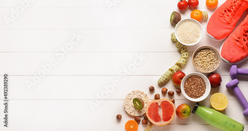 Different healthy products, shoes, dumbbells and measuring tape on white wooden background