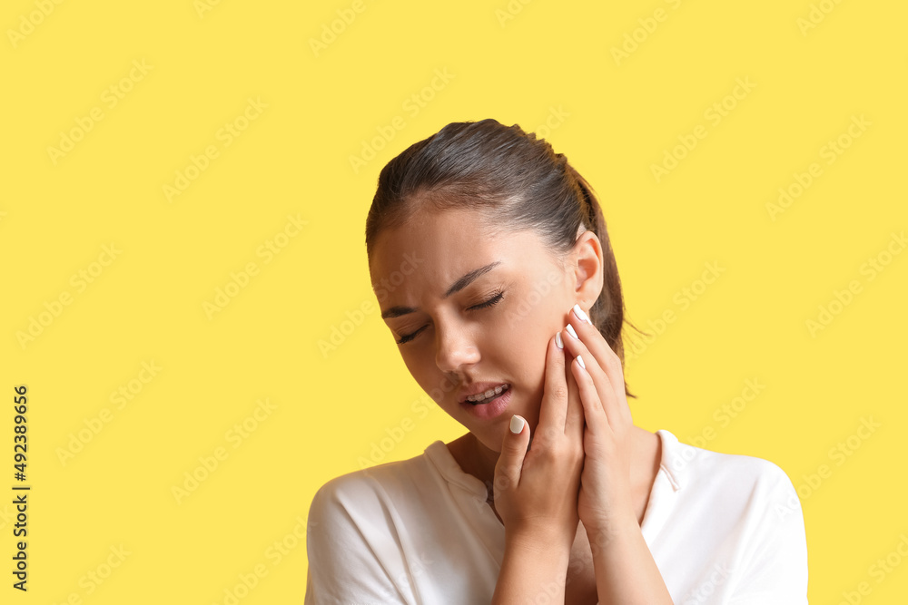 Pretty teenage girl with dental braces suffering from toothache on yellow background Pretty teenage girl with dental braces suffering from toothache on yellow background