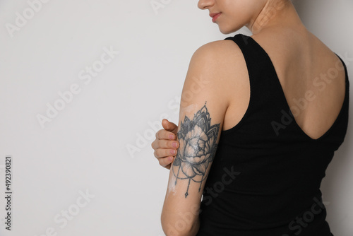 Woman applying cream onto her arm with tattoo on white background, closeup. Space for text