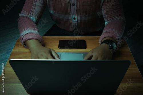 A man is sitting on a laptop in a dark room with lights shining down on it.internet concept addiction.topview. photo