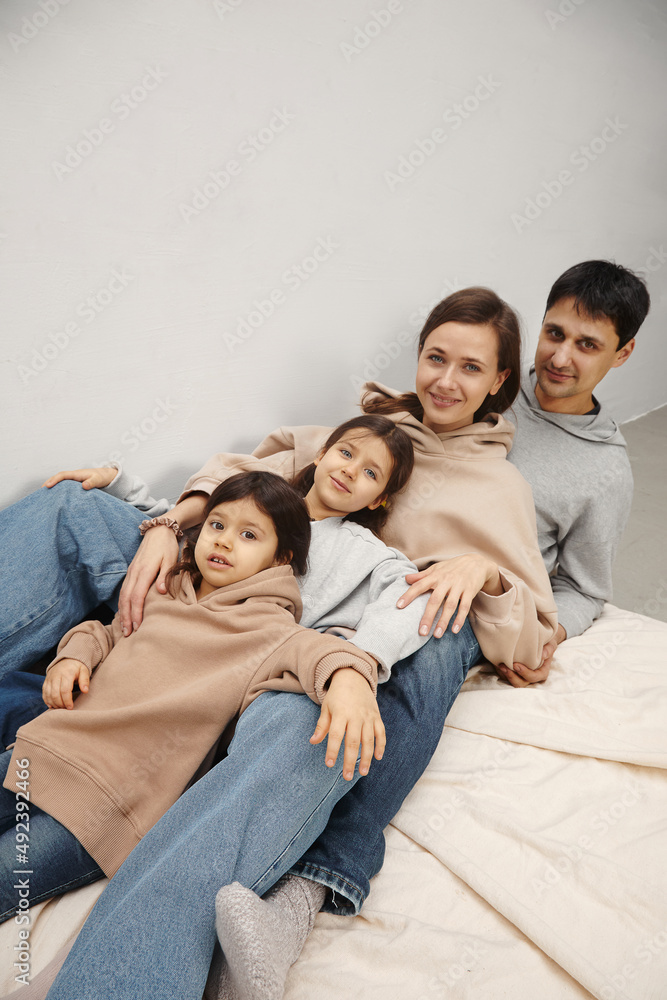 Portrait of happy caucasian parents posing with their little daughters at home, beige pastel background Portrait of happy caucasian parents posing with their little daughters at home, beige pastel background