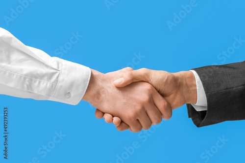 Business men shaking hands on blue background, closeup