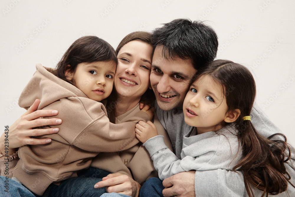 Portrait of happy caucasian parents posing with their little daughters at home, beige pastel background