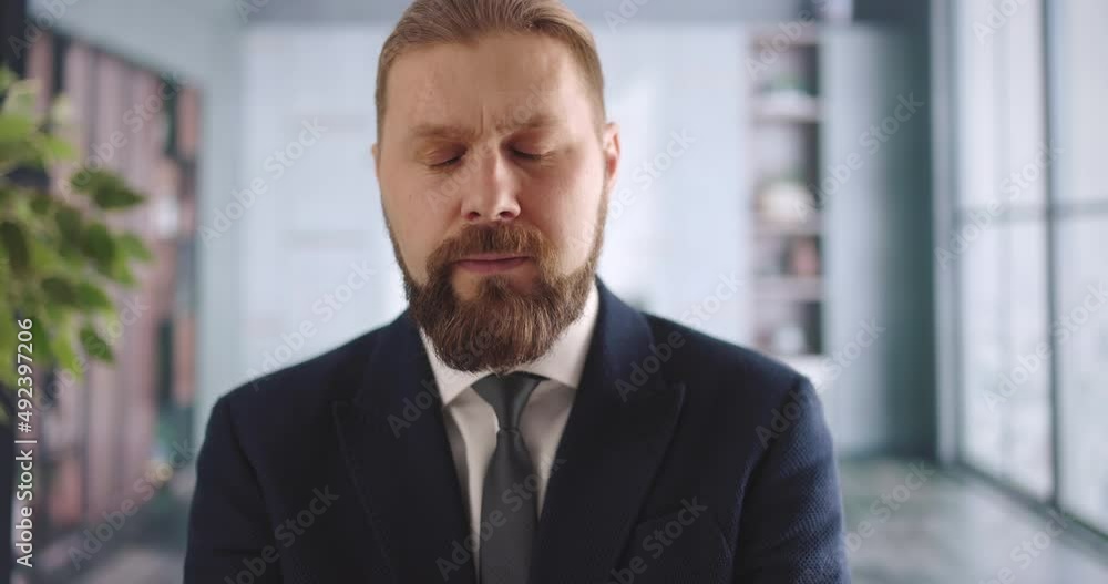 Portrait of bearded man in stylish suit and tie talking confidently while sitting at office desk. Successful businessman having conference call with colleagues online. Portrait of bearded man in stylish suit and tie talking confidently while sitting at office desk. Successful businessman having conference call with colleagues online.