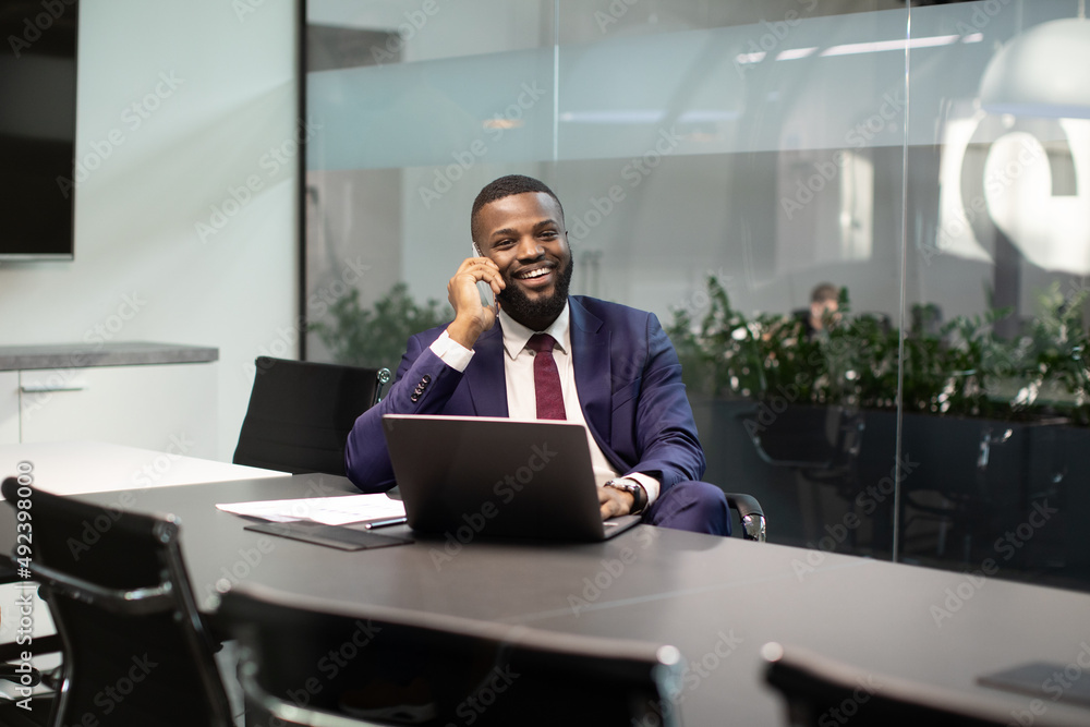 Positive black manager working on computer, having phone conversation Positive black manager working on computer, having phone conversation
