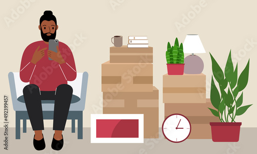 A man at home with a mobile phone sits in a chair. The concept of online registration of delivery of boxes, goods and assistance in moving.