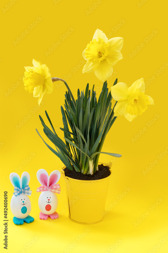 Beautiful yellow daffodils in bucket and two toy easter bunnies on paper background. Beautiful yellow daffodils in bucket and two toy easter bunnies on paper background.