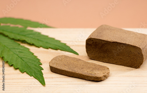 hashish tablet, hashish portion 100 grams, with large marijuana leaf, on wood, brown background