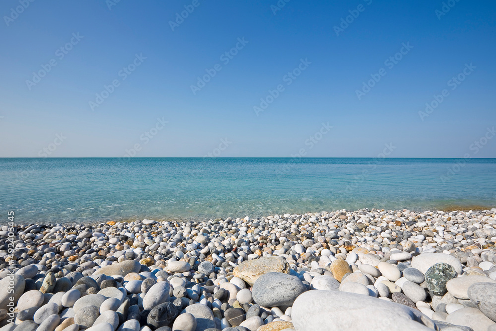 White and gray stones softly rounded and washed from sea water with horizon over the sea and cloudless sky White and gray stones softly rounded and washed from sea water with horizon over the sea and cloudless sky