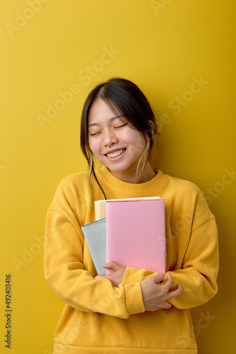 Portrait young happy asian woman hugging books reading education studying learning knowledge smiling positive emotion, in casual yellow shirt, Yellow background isolated studio shot and copy space.