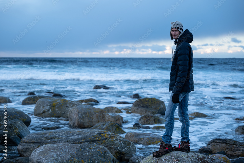 Person standing on stones at norways winter coast - sunset