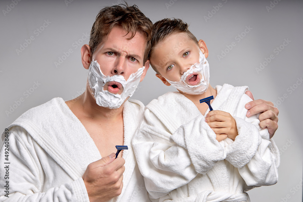 joyful Man and little boy having fun with shaving foam on faces in bathroom, isolated. Funny Happy Father and son shaving faces in the morning together, making crazy faces, weekends