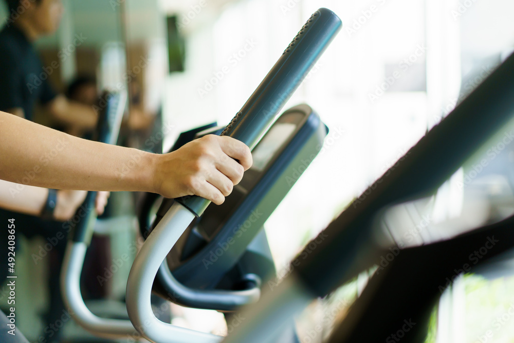 Active Asian young man making a cardio exercise on the elliptical exercise machine in the gym. 