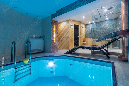 A small private pool in blue tones in a room with a wooden sauna and a shower cabin.