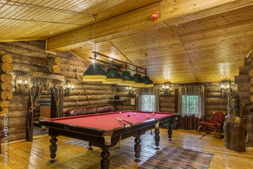Billiard room in the interior of a log wooden house. A table with pink cloth. The decor is in the ethnic style.
