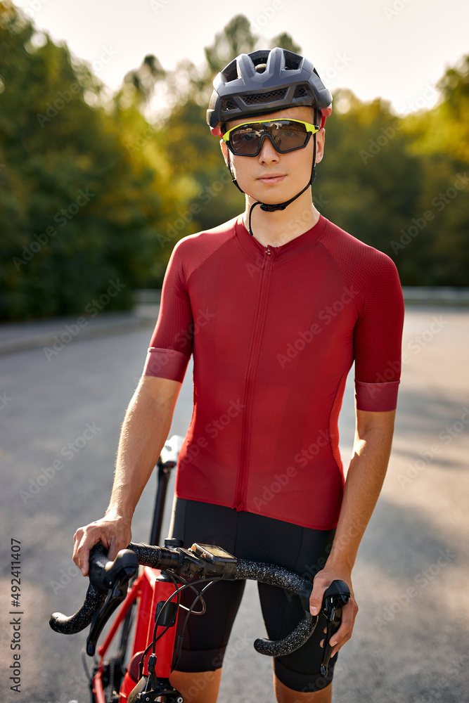 Athlete caucasian guy biker in cycling clothes and helmet with bicycle, looking at camera. Man resting and relaxing after work, training on bicycle on nature park streets. Healthy lifestyle Athlete caucasian guy biker in cycling clothes and helmet with bicycle, looking at camera. Man resting and relaxing after work, training on bicycle on nature park streets. Healthy lifestyle