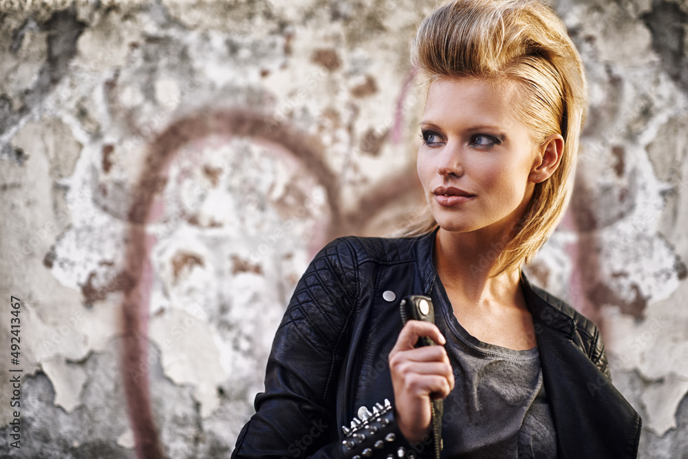 Rocknroll fashion. An edgy young woman holding the collar of her leather jacket.