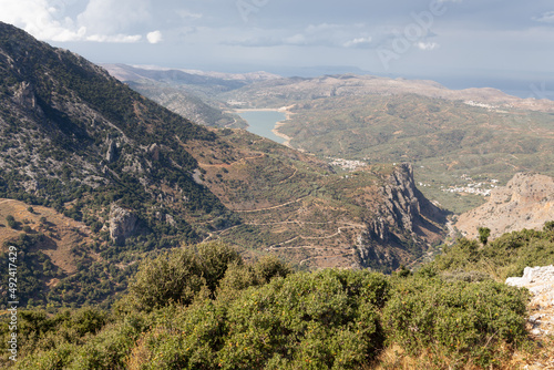 Landscape of valley with rocks, bushes, winding road and lake disappearing in haze, Crete, Greece