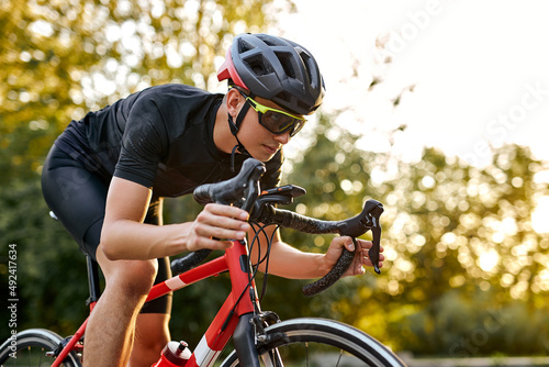 Cyclist riding a bike on an open road, Biking cyclist male athlete training hard on bicycle outdoors at sunset. Nature landscape. confident and concentrated man in black sportswear in helmet photo