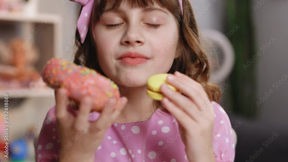 Close up of attractive school girl on home background, licks her lips, sniffing donut and yellow macaron, closes her eyes with pleasure. Dessert person, sweet tooth, gourmet. Feeling good, delicious Close up of attractive school girl on home background, licks her lips, sniffing donut and yellow macaron, closes her eyes with pleasure. Dessert person, sweet tooth, gourmet. Feeling good, delicious
