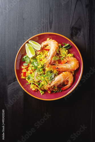 Spanish paella with seafood on the red teralke with lime. Delicious lunch on the shore of the sea shrimp. Dark wood background. Top view