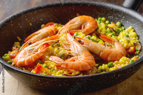 Spanish paella with seafood in a frying pan. Delicious lunch on the shore of the sea shrimp. Dark wood background.