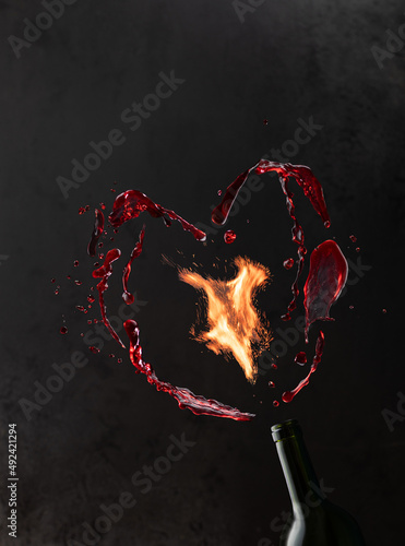 Bottle of wine with flying splashes of liquid and sparks of burning fire on black background with copy space.Drink and fire in freeze moition.Close up. photo