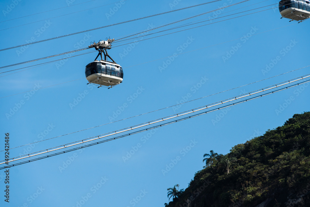 Pão de Açucar cable car passing with the hill in the background. Neighborhood of Urca, in Rio de Janeiro, Brazil. Sunny day at dawn. Blue sky