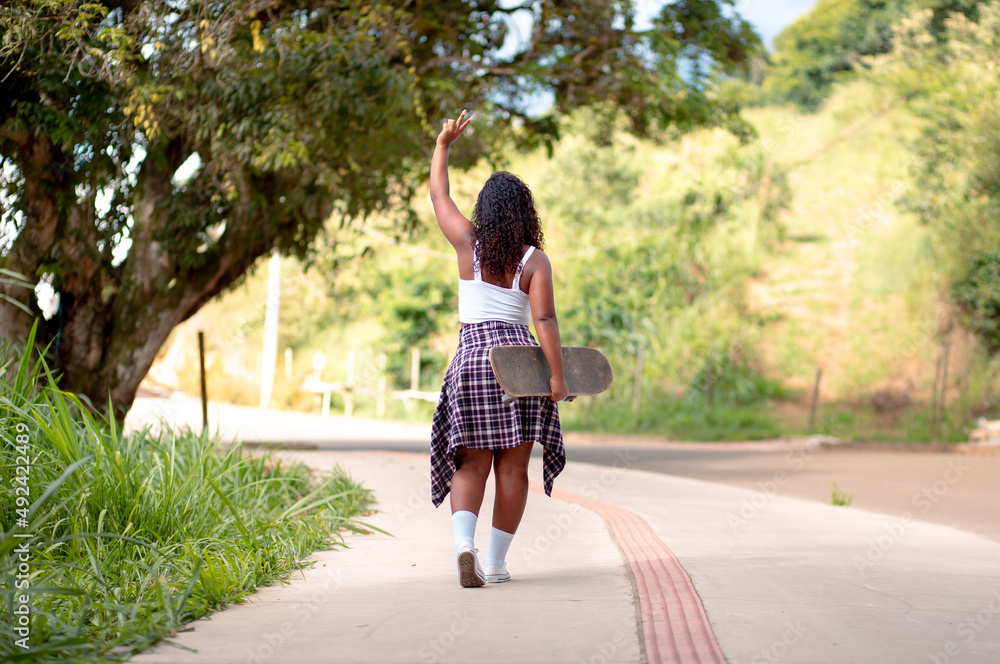 Young black woman holding a skateboard and walking on the street Young black woman holding a skateboard and walking on the street