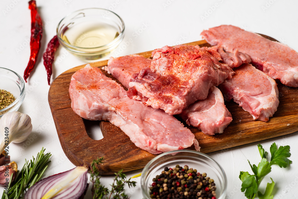 Raw meat steaks on a cutting board. White background. Preparation for cooking pork meat. Various spices, seasonings lie nearby. Raw meat steaks on a cutting board. White background. Preparation for cooking pork meat. Various spices, seasonings lie nearby.