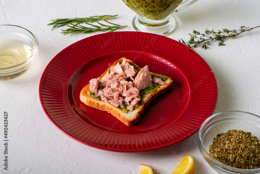 Toast with tuna and chimichurri sauce on a red plate. White background.