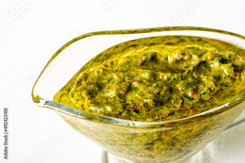 Chimichurri sauce in a gravy bowl on a white background. Argentinean vegetarian sauce made from olive oil, oregano, parsley.