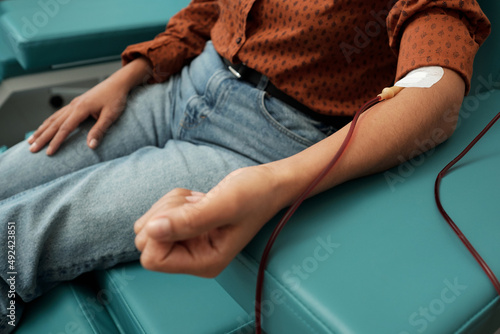 Close-up of young female donor in casual clothes giving her blood through hemotransfusion procedure in red zone of hospital photo