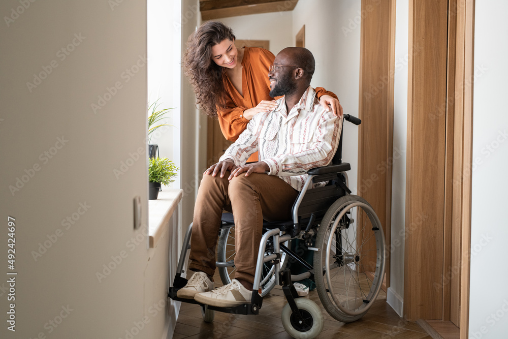 © pressmaster - Happy young man with disability looking at his affectionate caregiver while talking to her in front of window in corridor © pressmaster - Happy young man with disability looking at his affectionate caregiver while talking to her in front of window in corridor