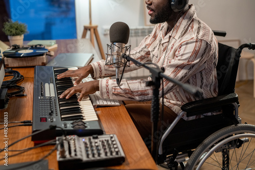 Mid section of African American performer with disability playing piano keyboard and singing while recording his music and songs