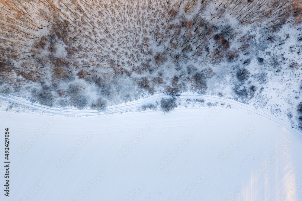 Aerial top down drone view of a road on winter snow covered fields and forest at sunset