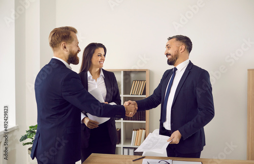 Smiling businesspeople shake hands close deal or make agreement at meeting in office. Happy diverse business partners handshake get acquainted greeting at negotiations. Partnership concept.