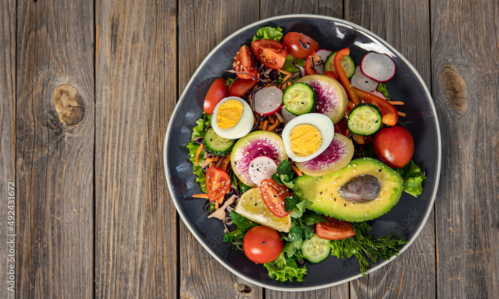 Appetizing vegetable salad with eggs, avocado on a wooden background.