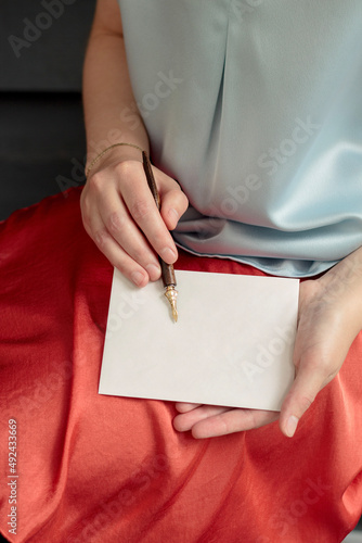 Woman's hands holding a blank card and fountain pen close up with orange skirt and blue shirt.