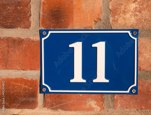 House number eleven on red brick wall | white on blue enamel sign photo