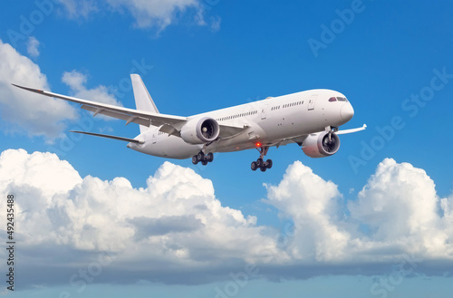 Passenger plane with landing gear lowered before boarding at the airport on a background of clouds and blue sky.