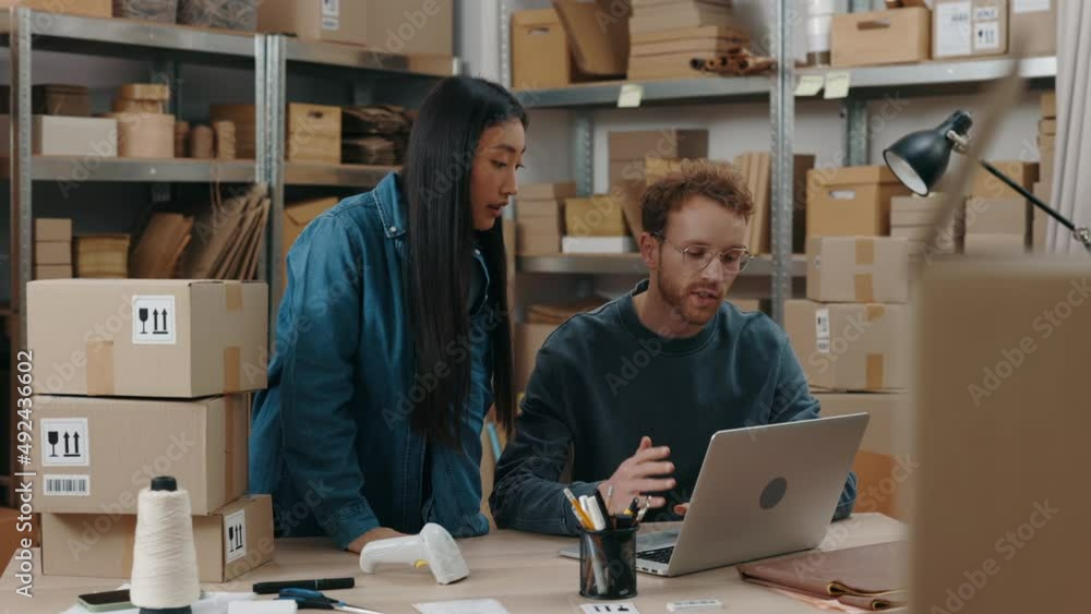 Asian woman putting at the laptop screen with her finger while discussing something with her caucasian colleague while they working at the home office. Small business concept. Asian woman putting at the laptop screen with her finger while discussing something with her caucasian colleague while they working at the home office. Small business concept.