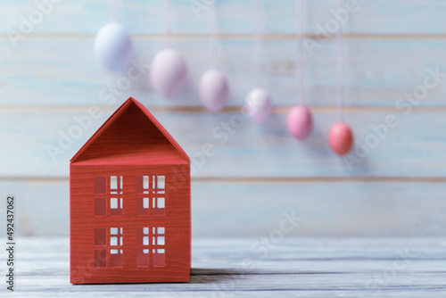 Red toy house over defocused Easter eggs on light wooden background photo