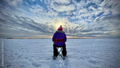 A person sitting in a chair ice fishing on a frozen lake in Newell County Alberta Canada under a dramatic sunset sky.
 photo