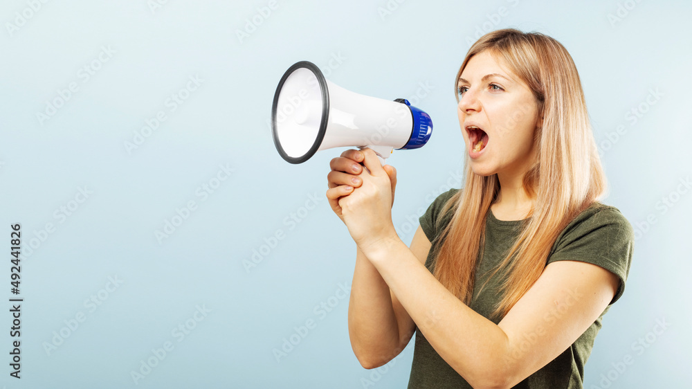 Young blonde woman shouting loudly while holding a megaphone on blue background. Concept of speech and announce, idea for marketing or sales Young blonde woman shouting loudly while holding a megaphone on blue background. Concept of speech and announce, idea for marketing or sales