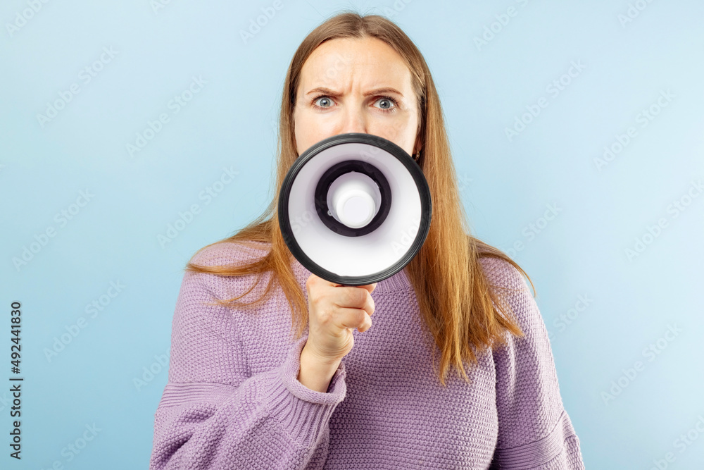Young brunette woman shouting loudly while holding a megaphone on blue background. Concept of speech and announce, idea for marketing or sales Young brunette woman shouting loudly while holding a megaphone on blue background. Concept of speech and announce, idea for marketing or sales