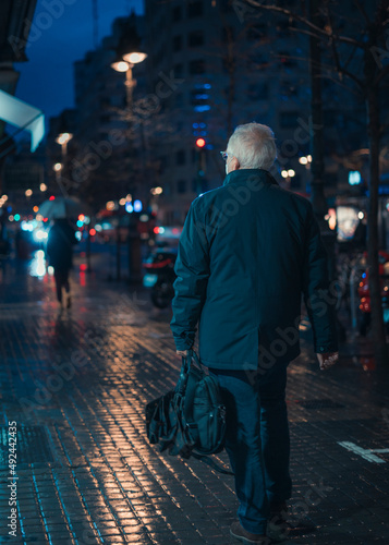 Old man walks at night in the rain